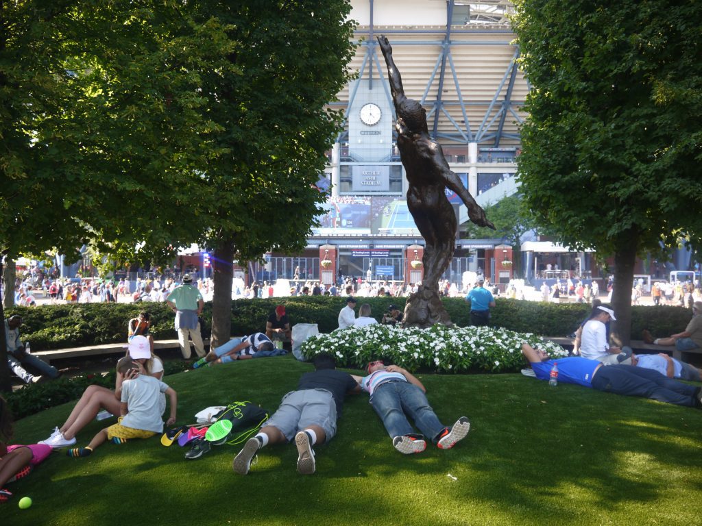 Fans descansan en el jardín dedicado al legendario Arthur Ashe con la vista al imponente estadio que lleva su nombre.