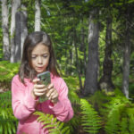 Una niña usando un smartphone en el bosque.