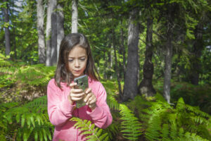 Una niña usando un smartphone en el bosque.