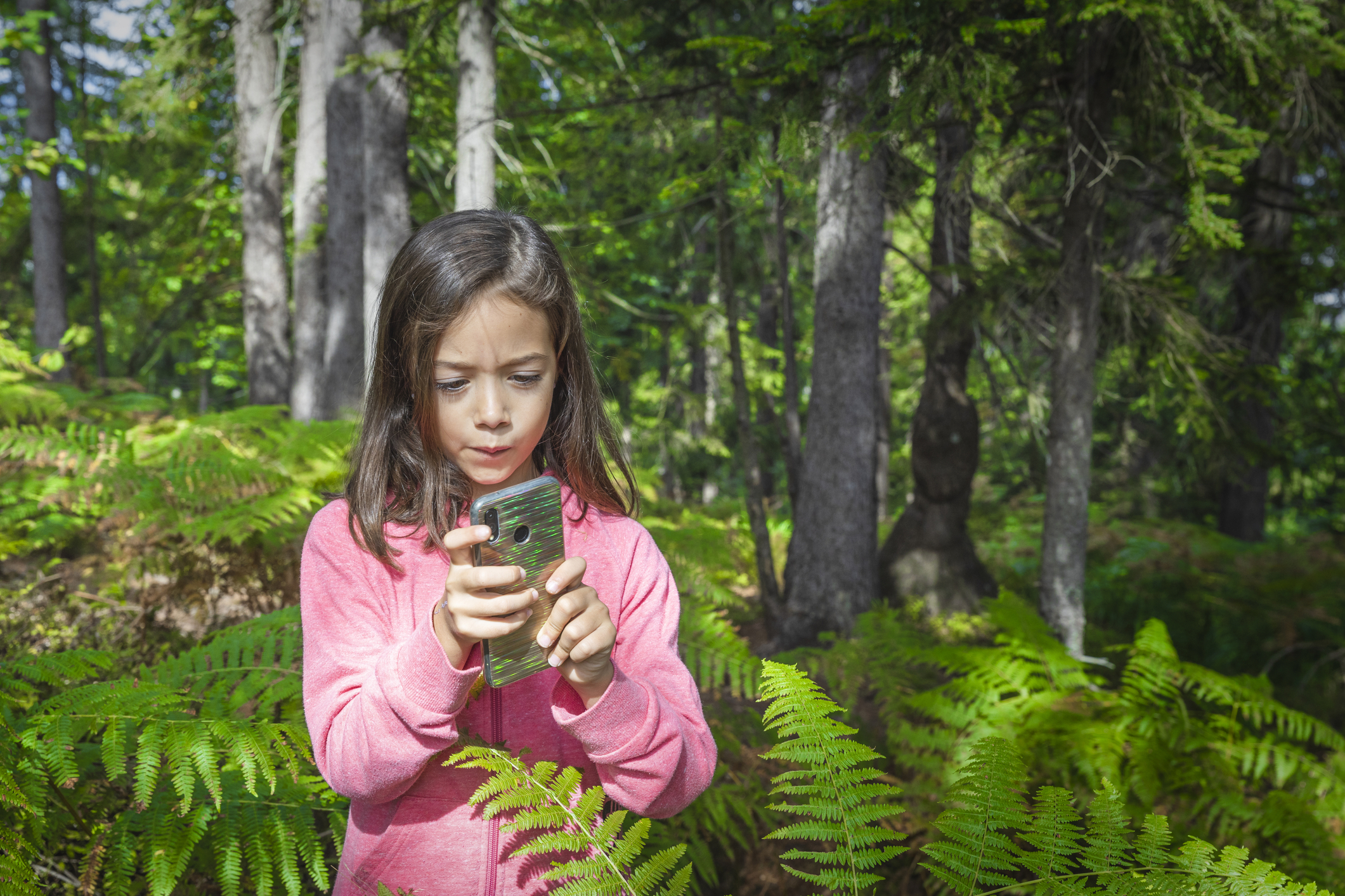Una niña usando un smartphone en el bosque.